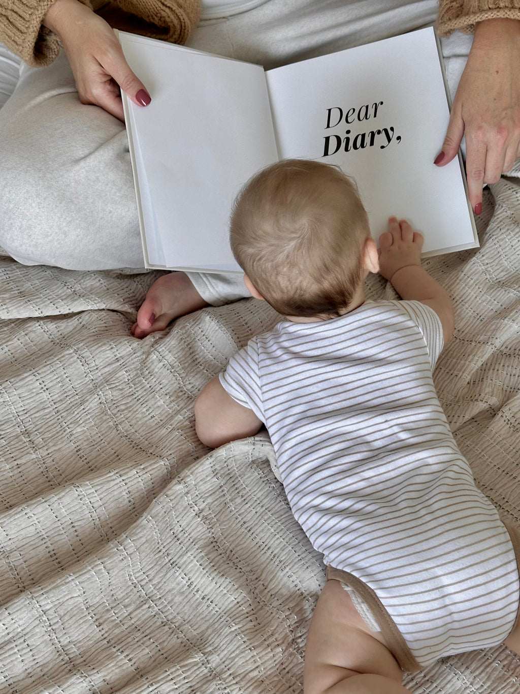 Baby looking at the open Dear Diary memory book while sitting with a paren